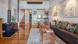 A spacious living area with a fireplace, a sofa, a coffee table, and a kitchen in the background. - Taman Sari Luxury Private Pavilions (Mapleton)