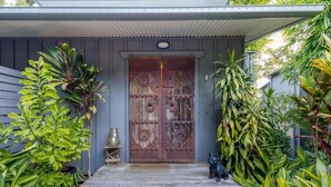 A wooden deck leading to a rustic door with intricate metalwork, surrounded by lush green plants. - Taman Sari Luxury Private Pavilions (Mapleton)