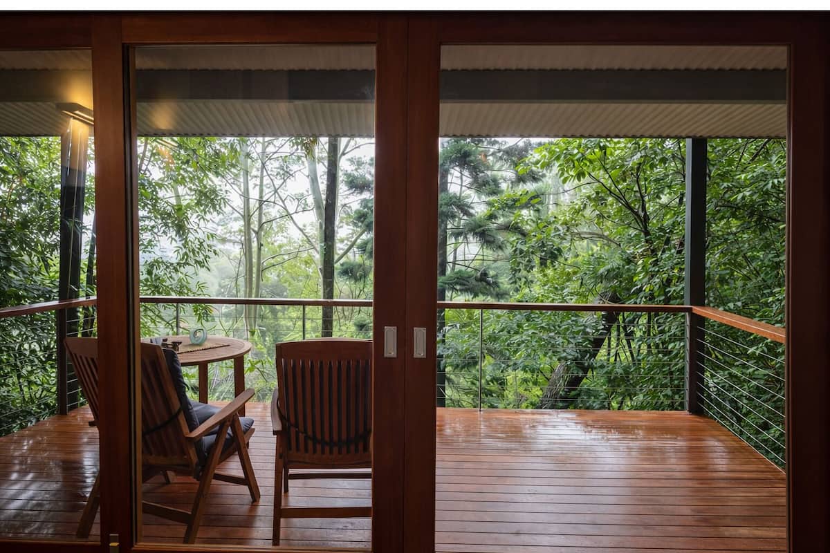 A wooden deck with a table and chairs, overlooking a dense forest.