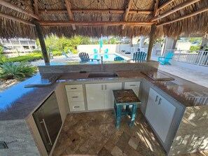 An outdoor kitchen area with a thatched roof, a sink, and a small stool. - Sombrero Beach Golfside Tropical Retreat With Heated / Cooled Pool (Marathon)