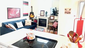 A living room with a blue sofa, a white table with a floral teapot, a guitar, and various decorations. - On Razorback Trail!  Walk to Dickson, Stadium & UARK (Fayetteville)