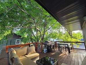 Een houten terras met een bank, een barbecue en een tafel.