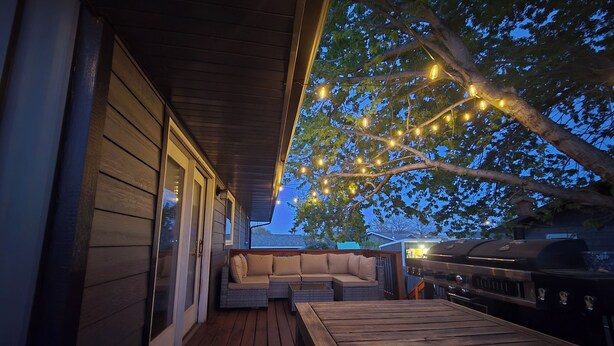 Ein überdachter Außenbereich mit Holzterrasse, Grill und Lichterkette.