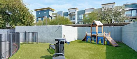 A fenced backyard with artificial grass, a play structure, and a bench.