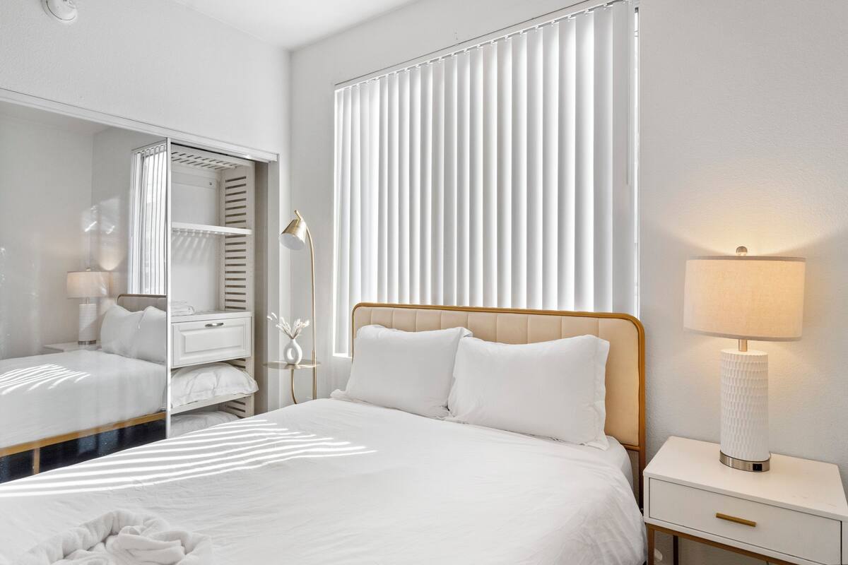 Une chambre d’hôtel bien rangée, avec un lit, une table de chevet, une lampe et un miroir.