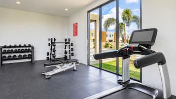 A gym with a treadmill, weight bench, dumbbells, and a squat rack.