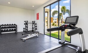 Une salle de sport équipée d’un tapis de course, d’un banc de musculation, d’haltères et d’un support à squats.