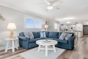 A modern living room with a blue sectional sofa, a round coffee table, and a ceiling fan. - 3rd Floor 3BR 2BA @ Regency Towers Directly on the Beach!! (Panama City Beach)