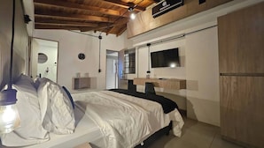 A bedroom with a bed, a TV, a wooden wardrobe, and a ceiling with exposed beams.