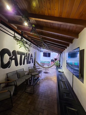 A cozy outdoor seating area with a hammock, a bar with a TV, and a large wall with the word "CATANA". - Aguacatala 6BR & Big Hot Tube (Medellín)