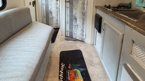 A compact RV interior with a kitchenette, a sofa, and a door leading to a bathroom. - StayNow @ The Mini Escape between New Braunfels & Canyon Lake (New Braunfels)