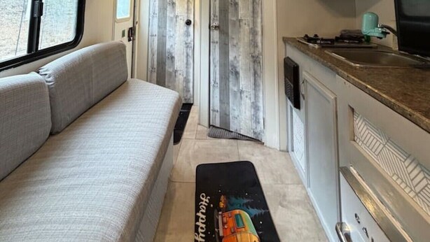 A compact RV interior with a kitchenette, a seating area, and a door leading to an exterior view. - StayNow @ The Mini Escape between New Braunfels & Canyon Lake (New Braunfels)