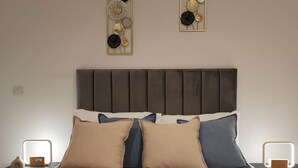 Quarto de hotel com cama, almofadas, mesa de cabeceira, relógio de parede e arte decorativa na parede.