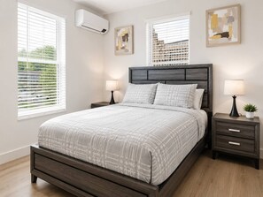Ein Schlafzimmer mit Bett, Nachttischen und einer Wand-Klimaanlage.