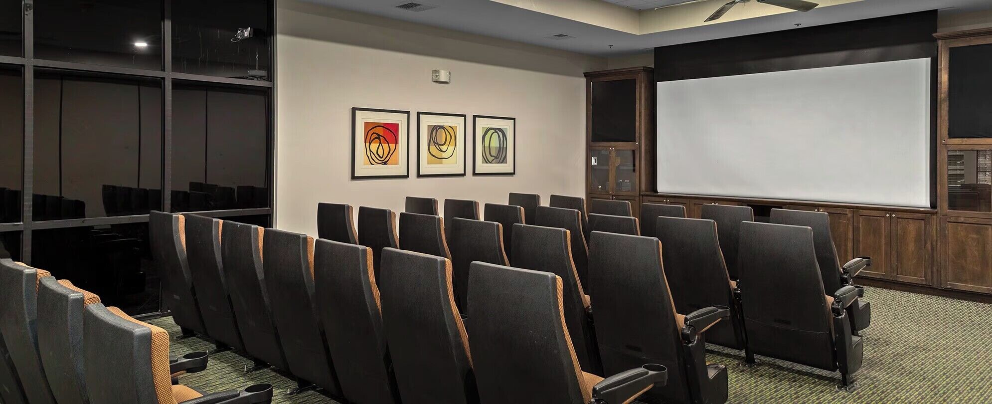 A conference room with rows of chairs, a projection screen, and three framed artworks on the wall.