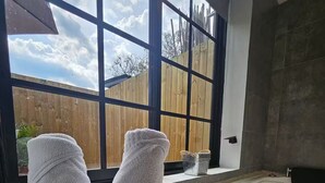 A bathroom with a large window, a bathtub, and a bucket labeled "FLOWERS & GARDEN" containing towels. - Party AGUA House Medellin 5BR w/5Hot tub (Medellín)