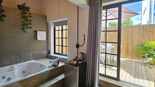 A modern bathroom with a large bathtub, a window, and a sliding glass door leading to an outdoor patio. - Party AGUA House Medellin 5BR w/5Hot tub (Medellín)