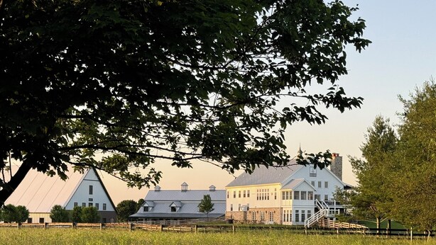 Un paysage rural avec une grande maison blanche, une grange et un champ.