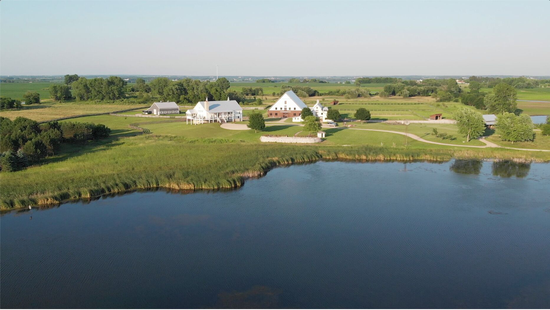 A large house with a pond in front, surrounded by green fields and trees.