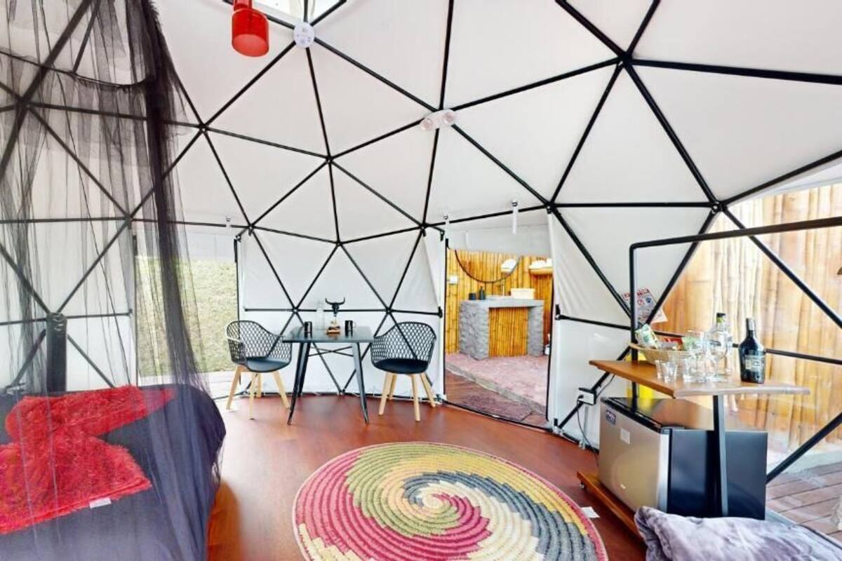 Habitación tipo tienda de campaña con cama, mesa de comedor con sillas, una pequeña cocina y una alfombra colorida.