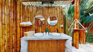 Un baño con pared de bambú, dos espejos redondos, una planta pequeña y un lavabo de piedra.
