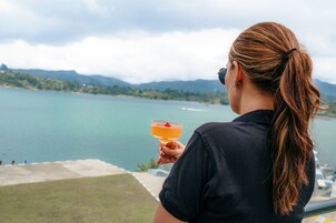 Una persona sosteniendo una bebida, con vistas a un lago y montañas al fondo.