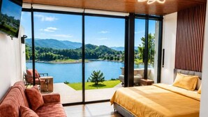 Un dormitorio con un ventanal grande, una cama, un sofá y vistas a un lago y montañas.