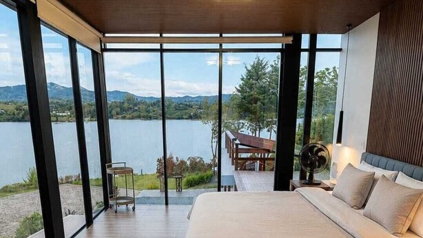 Un dormitorio moderno con una cama grande, vistas a un lago y un techo de madera.