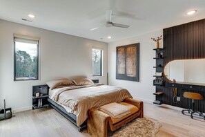 Un dormitorio moderno con cama, mesitas de noche, escritorio, silla, ventilador de techo y un ventanal grande.