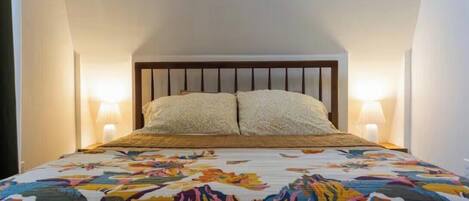 Un dormitorio con una cama, dos lámparas de noche y una colcha estampada con motivos florales.
