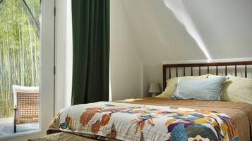 A bedroom with a bed, a bench, a window, and a view of greenery outside.