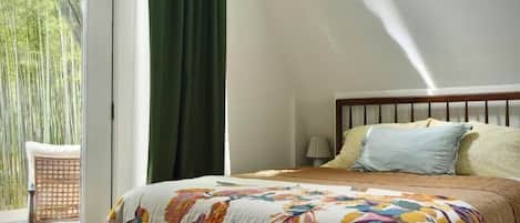 A bedroom with a bed, a bench, a window, and a view of greenery outside.
