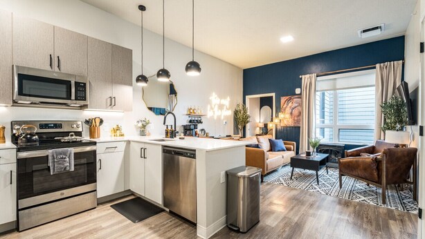 A modern kitchen with stainless steel appliances, a central island, pendant lighting, and a view of the living area with a sofa and a leather armchair. - Top Floor, Lounge, King Bed, BSU (Boise)