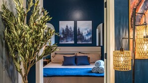 A bedroom with a bed, pillows, a blue blanket, and a wall-mounted lamp. - Top Floor, Lounge, King Bed, BSU (Boise)