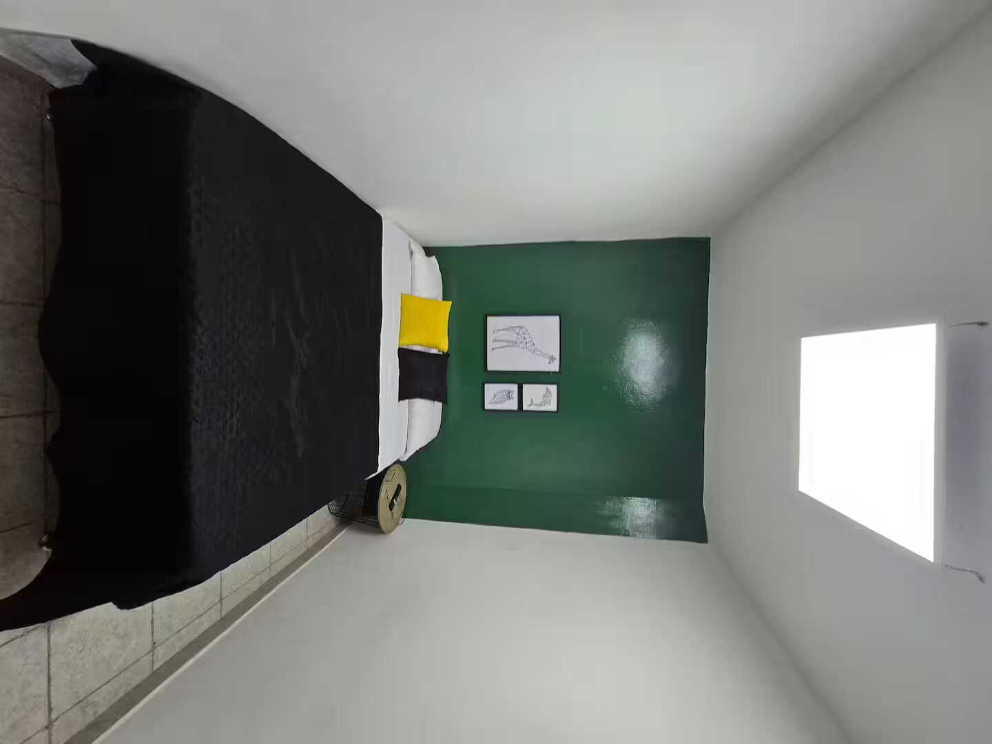 Un corridoio stretto con un letto a sinistra, un muro verde e una porta a destra.