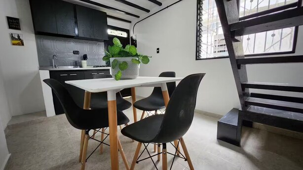 A modern kitchen with black cabinets, a white countertop, and a dining area with a white table and black chairs. - Prado House in Medellin 8BR & Terrace (Medellín)