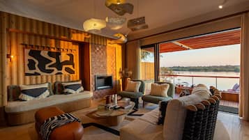 A modern living room with a large window overlooking a body of water, a fireplace, and a variety of seating options.