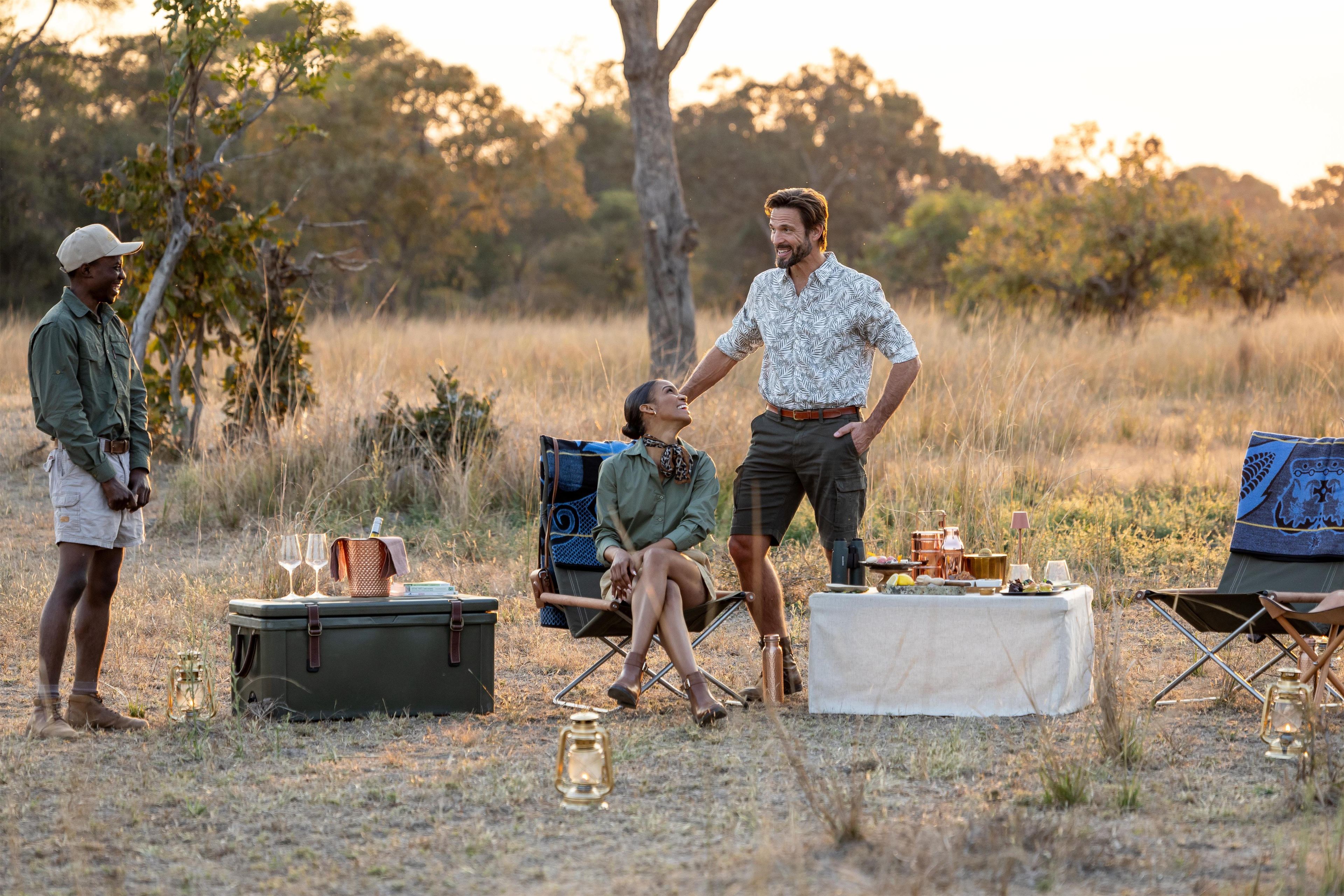 Une scène en plein air avec du matériel de camping, une table garnie de nourriture et une personne debout.