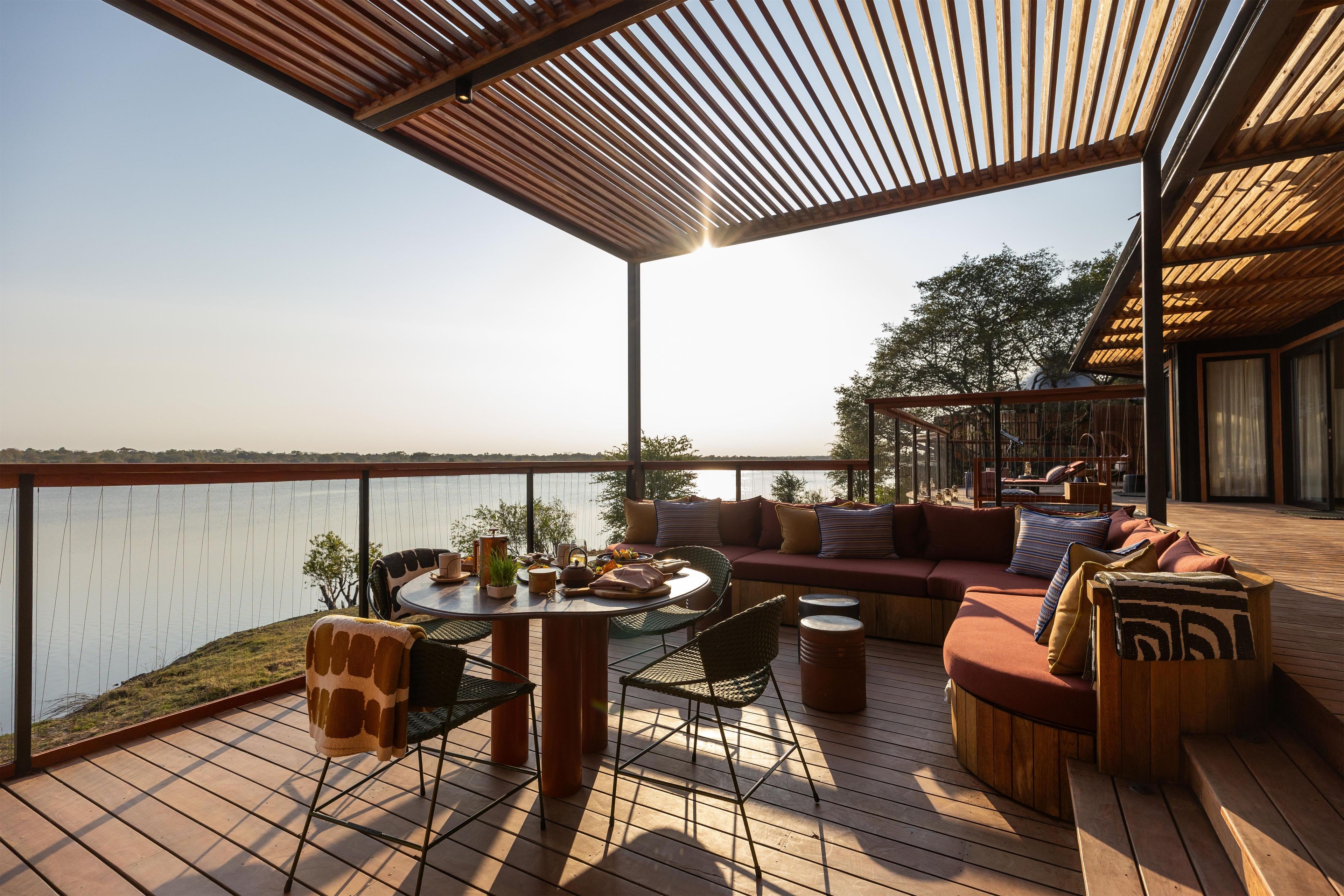 A deck with a wooden table, chairs, and a sofa with cushions.