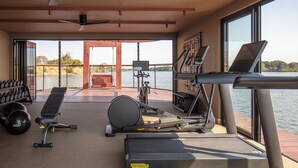 A gym with exercise equipment, a bench, and a view of the water. - Anantara Tented Camp Kafue River (Kafue National Park)