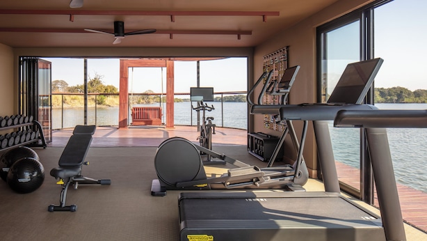 Ein Fitnessraum mit Trainingsgeräten, einer Bank und Blick auf das Wasser.