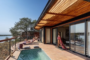 A modern outdoor deck with a pool, lounge chairs, and a view of the water. - Anantara Tented Camp Kafue River (Kafue National Park)