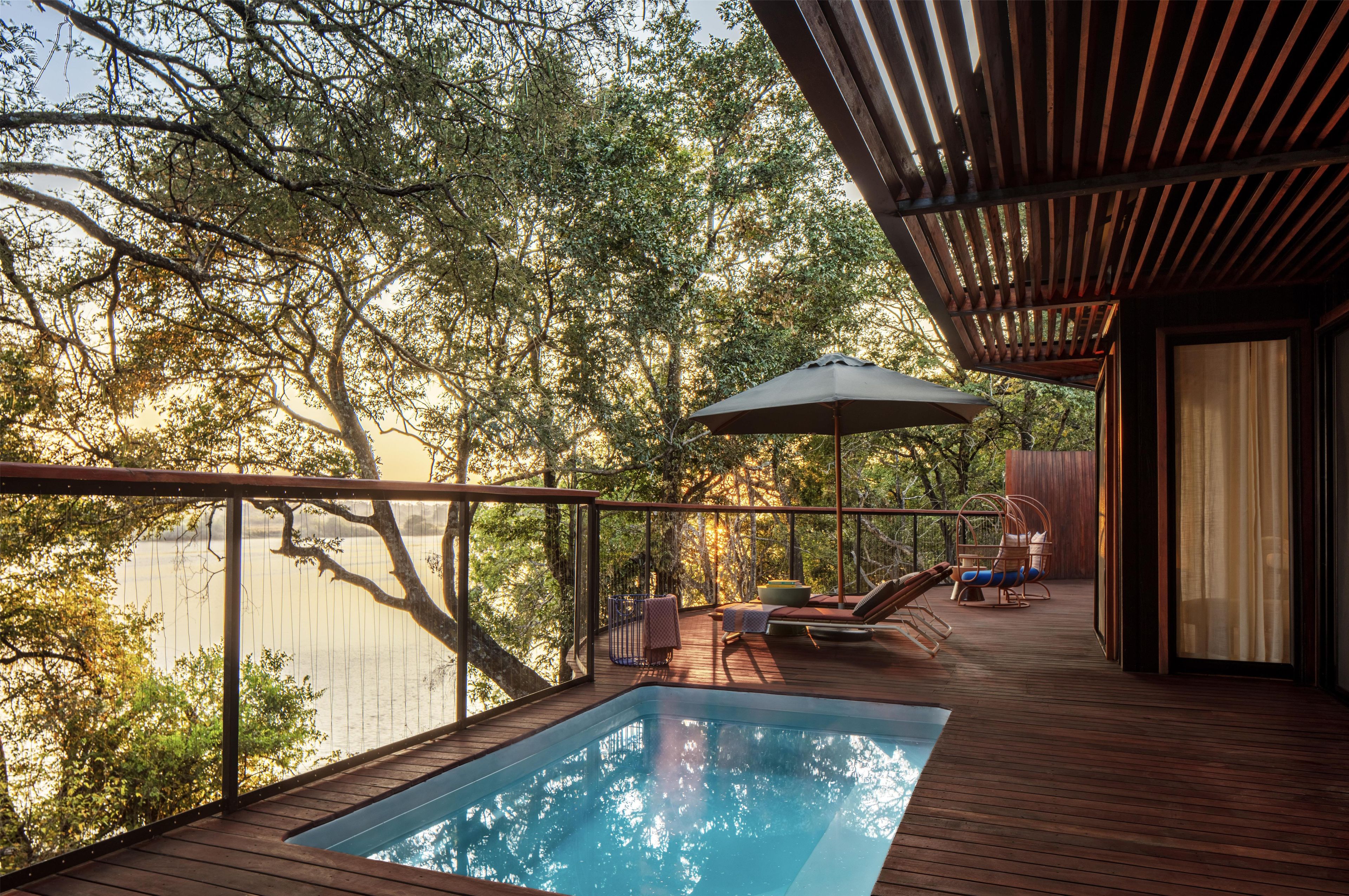 Una terraza de madera con piscina, sillones de descanso y un pérgola.