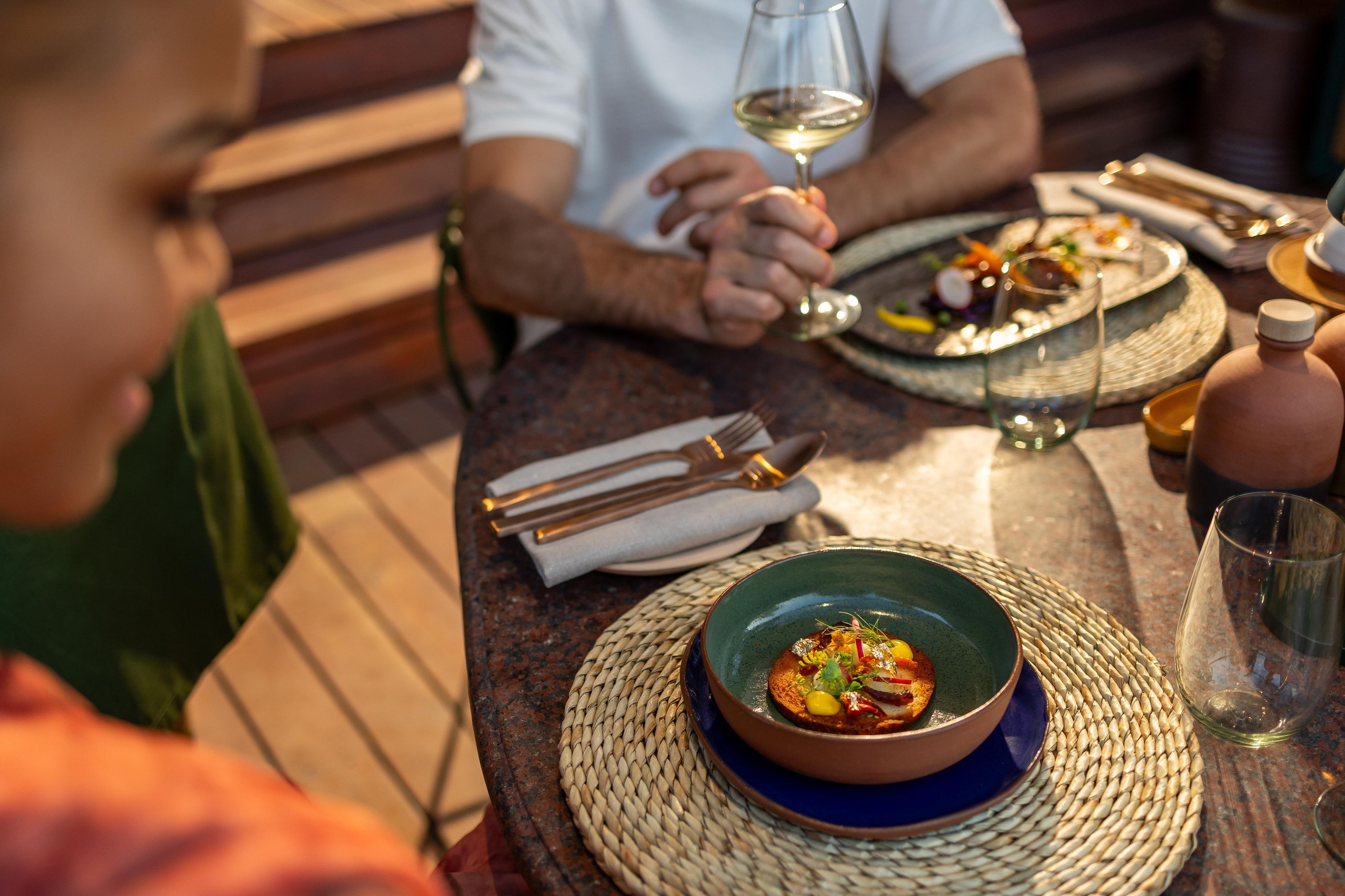 Una mesa con platos de comida, cubiertos y una copa de vino.