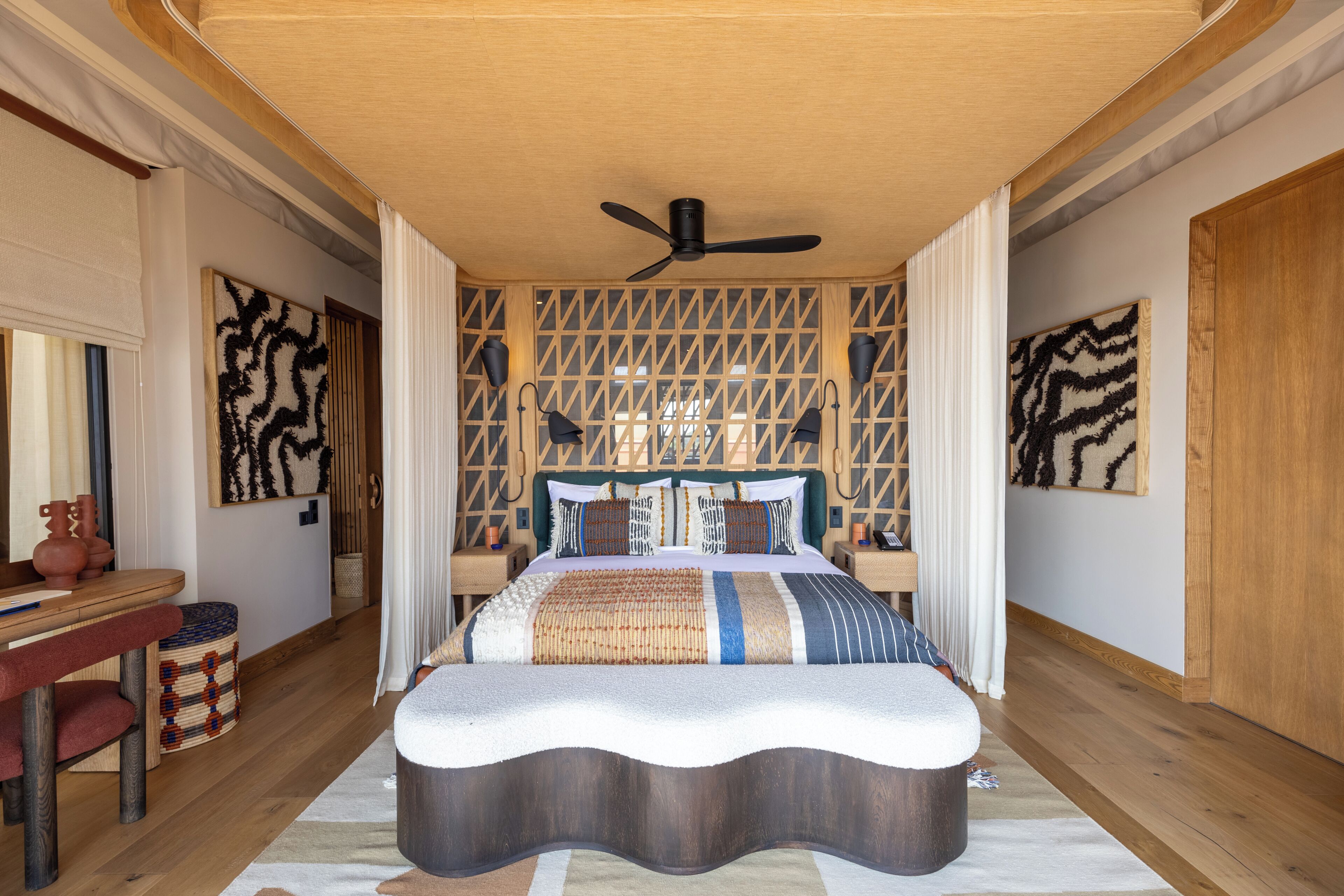 Un dormitorio con cama, ventilador de techo, cabecera de madera y pared con diseño.