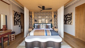 A bedroom with a bed, a ceiling fan, a wooden headboard, and a patterned wall. - Anantara Tented Camp Kafue River (Kafue National Park)