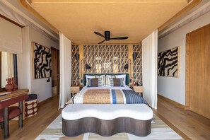 A bedroom with a bed, a ceiling fan, a wooden headboard, and a patterned wall. - Anantara Tented Camp Kafue River (Kafue National Park)