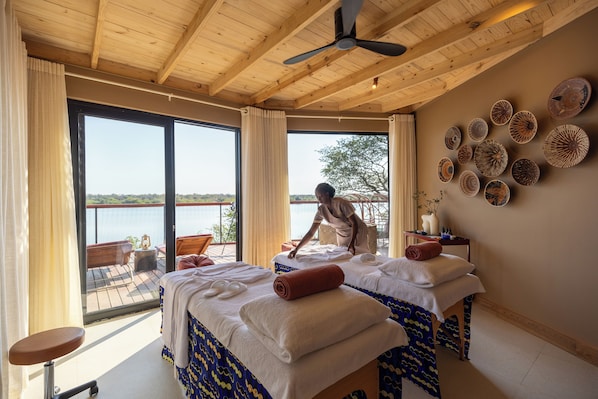 A room with two beds, a ceiling fan, large windows, and a view of the water.