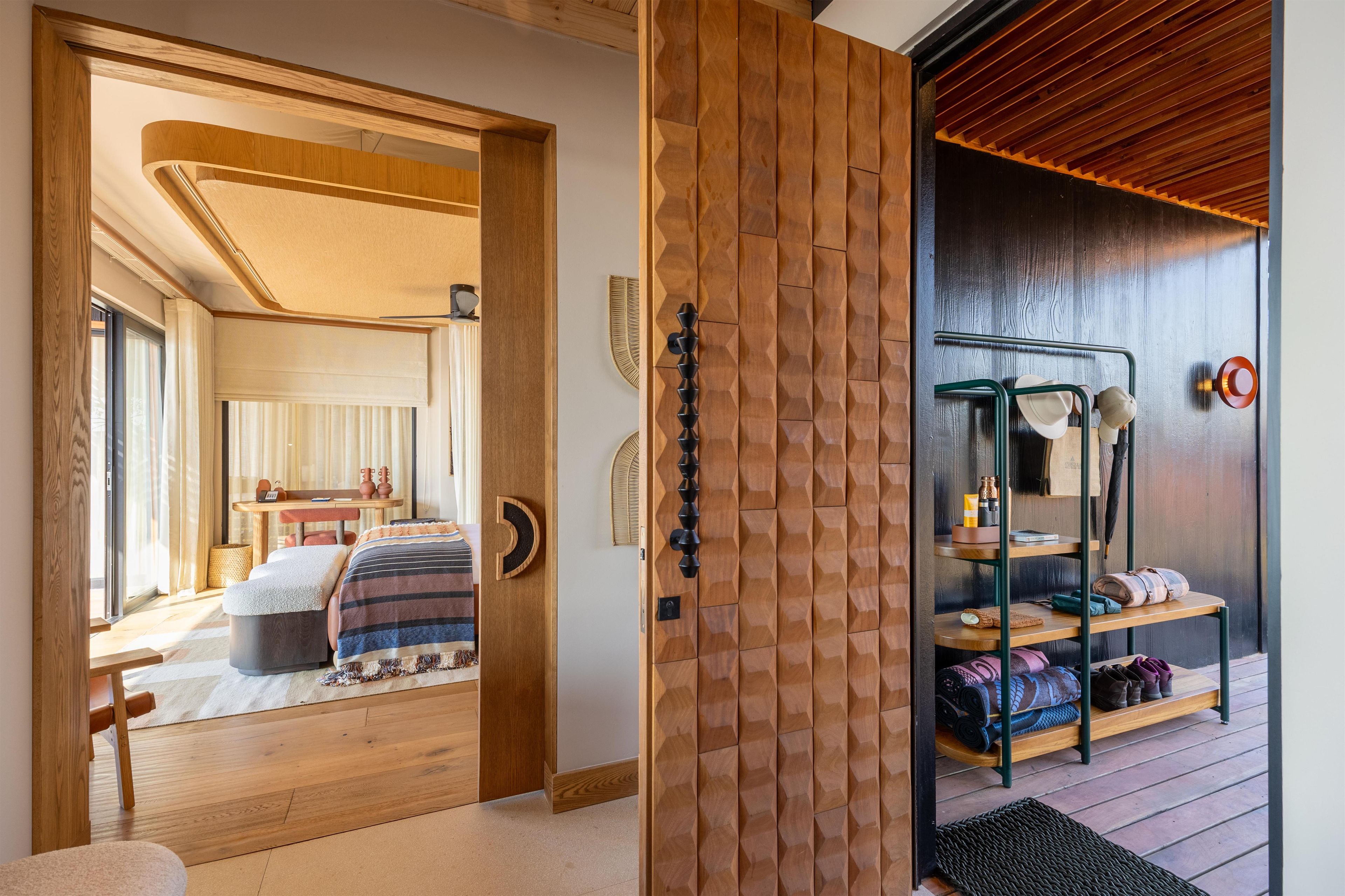 A modern interior with a wooden floor, a bed with a striped blanket, and a wooden door with a geometric pattern.