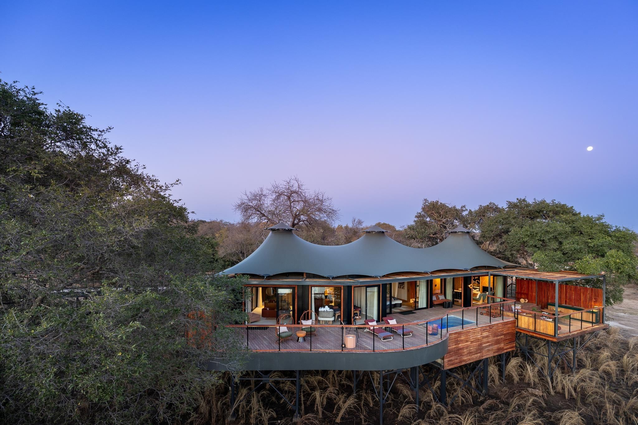 A modern, multi-level lodge with a large deck and pool, surrounded by dense vegetation.